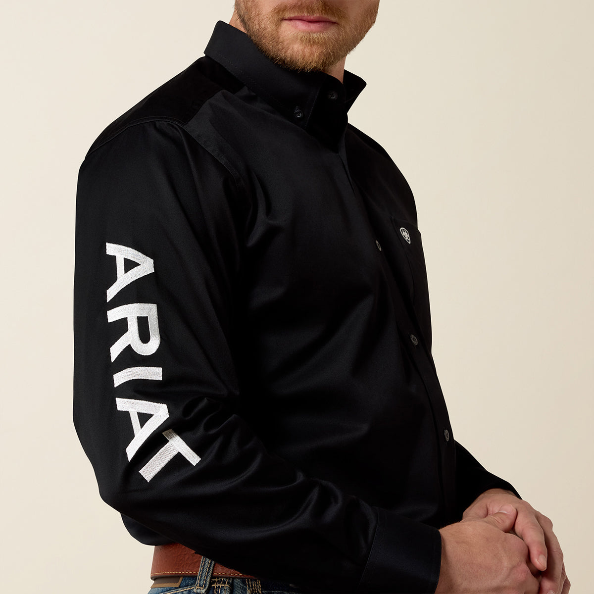 Man wearing a black long sleeve shirt with 'Ariat' branding on a beige background