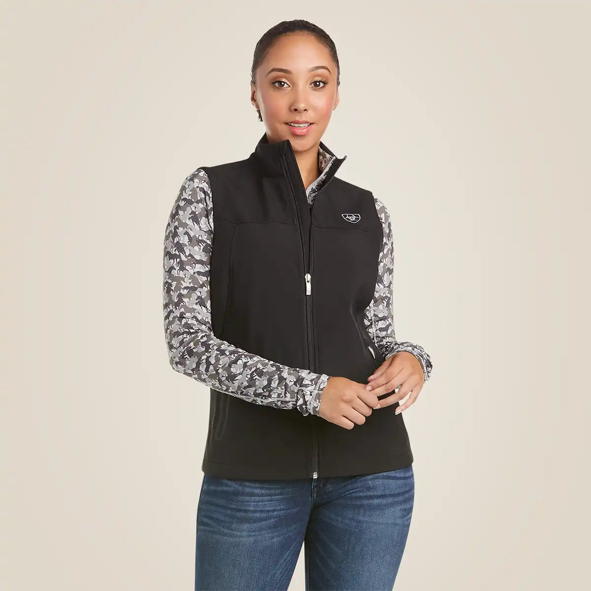 Front view of a woman wearing the Ariat Women's Black New Team Softshell Vest with white back logo embroidery.