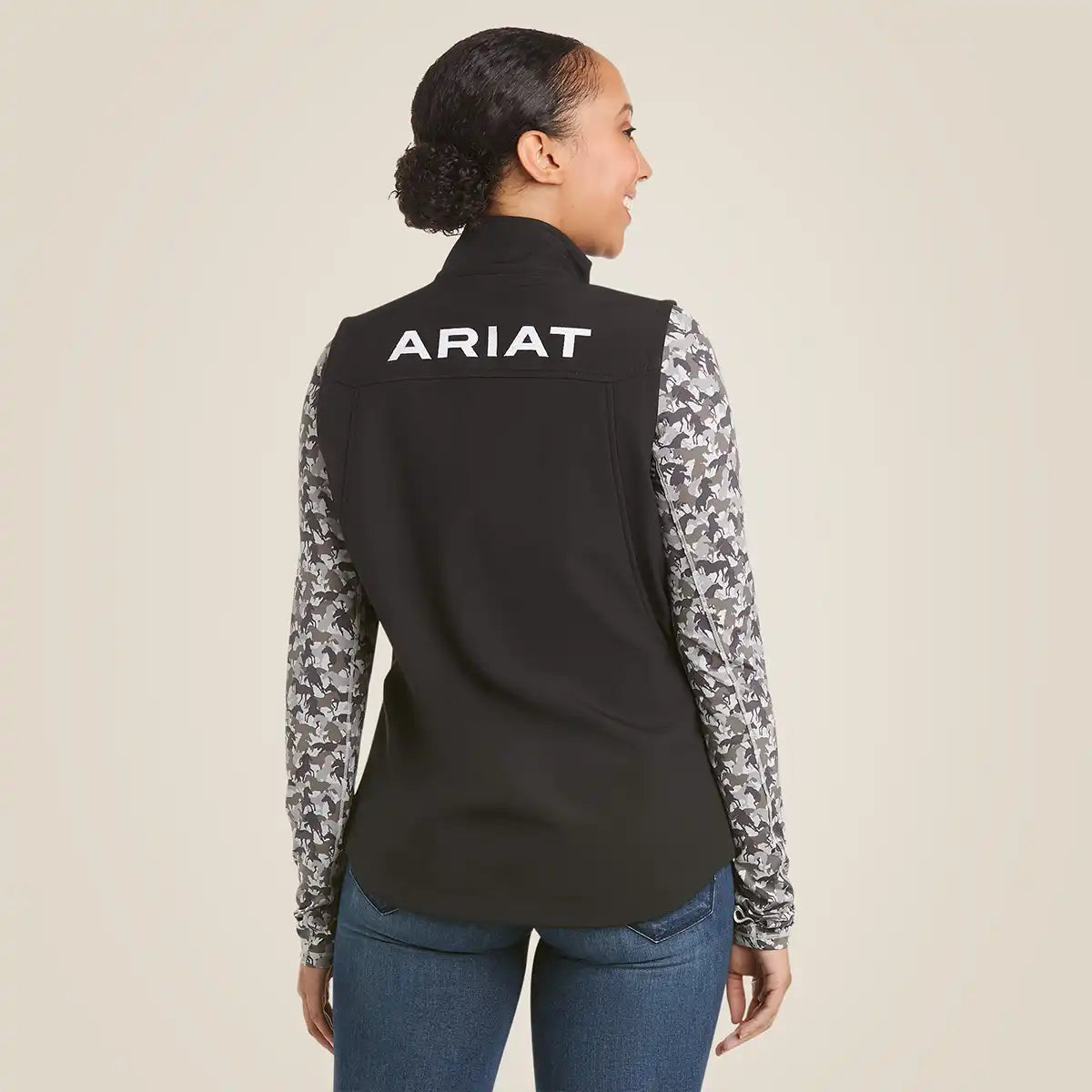 Back view of a woman wearing the Ariat Women's Black New Team Softshell Vest with white back logo embroidery.
