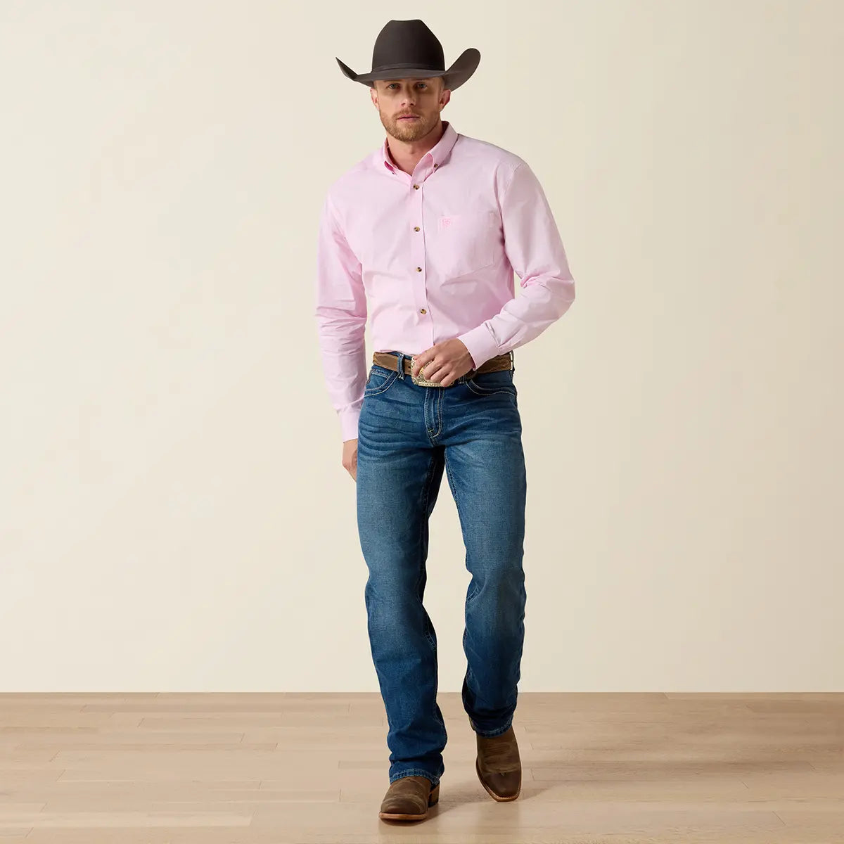 Full-length studio shot of the model wearing the Ariat Prism Pink Pro Series Dayne shirt, blue jeans, dark cowboy hat, and Western leather boots.