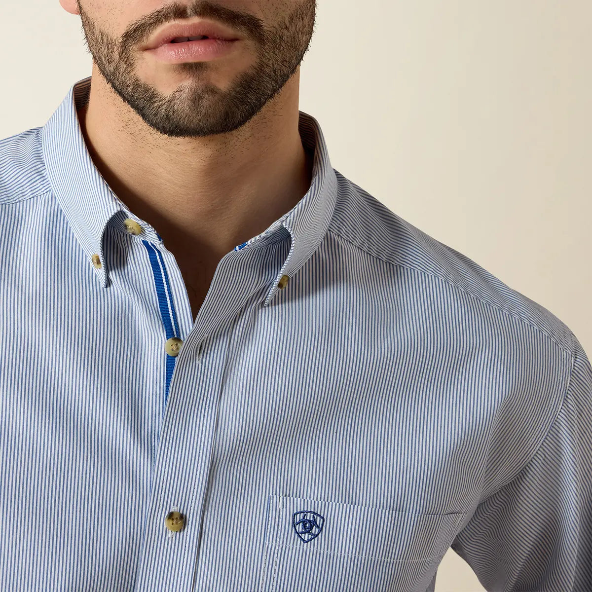 Close-up of the collar and chest on the Ariat Dayne shirt highlighting the royal blue inner placket accent, fine yarn-dye stripes, and blue logo embroidery.