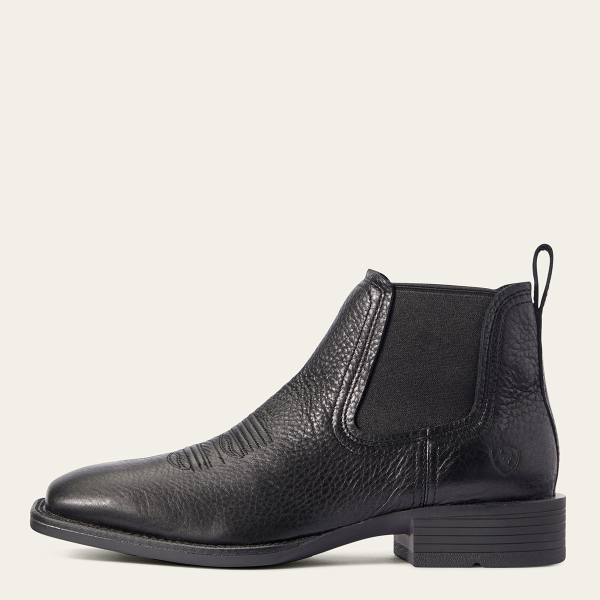 Ariat men's black leather Chelsea square toe boot with a textured pebbled finish, elastic side gore, and a low block heel, shown in profile against a light cream background.