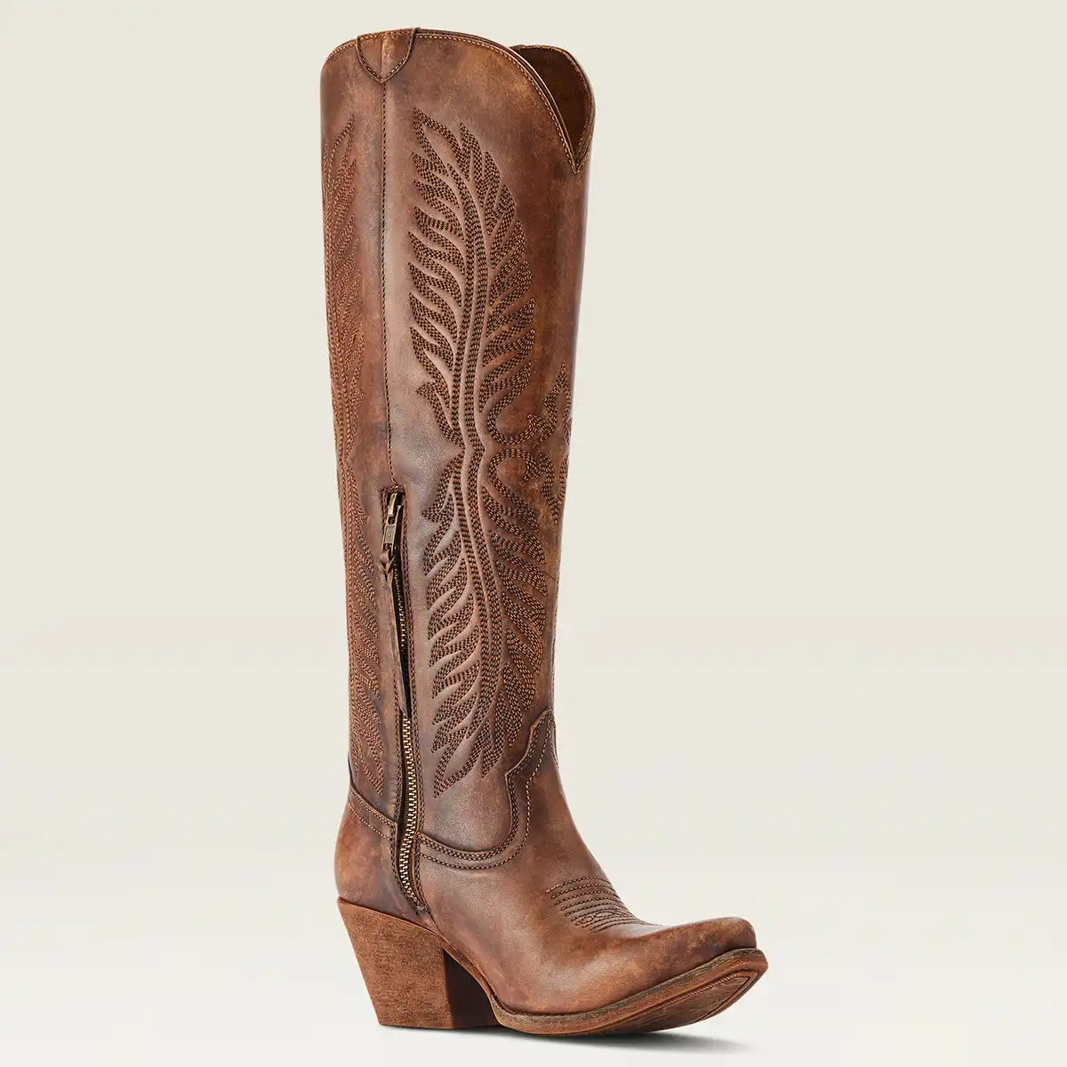A single women's brown leather knee-high Ariat cowboy boot with a pointed toe, stacked heel, and detailed western embroidery on the shaft, shown against a light beige background.