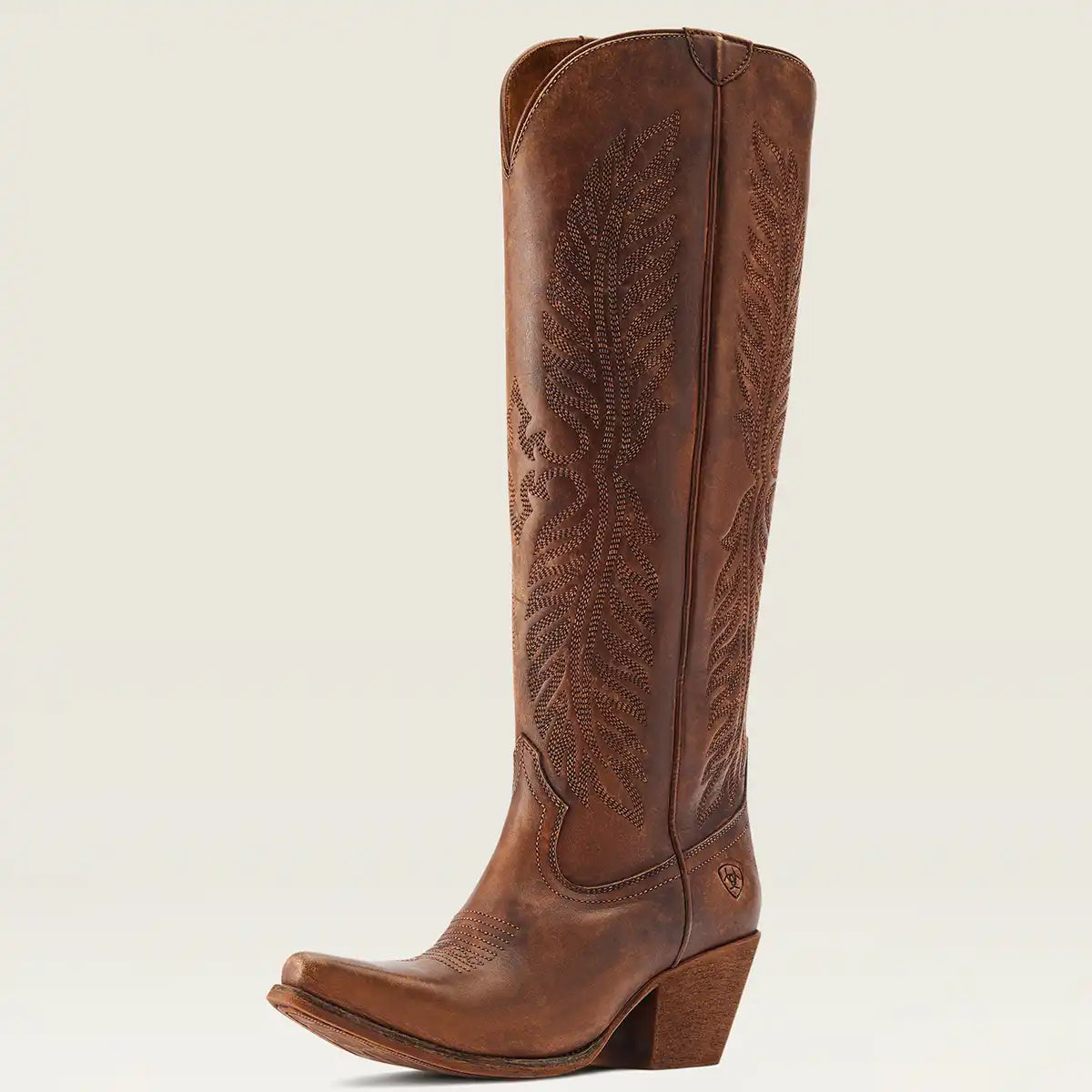 A single brown leather knee-high Ariat cowgirl boot with decorative tooling and stitching on the shaft, shown in a side profile against a light beige background.