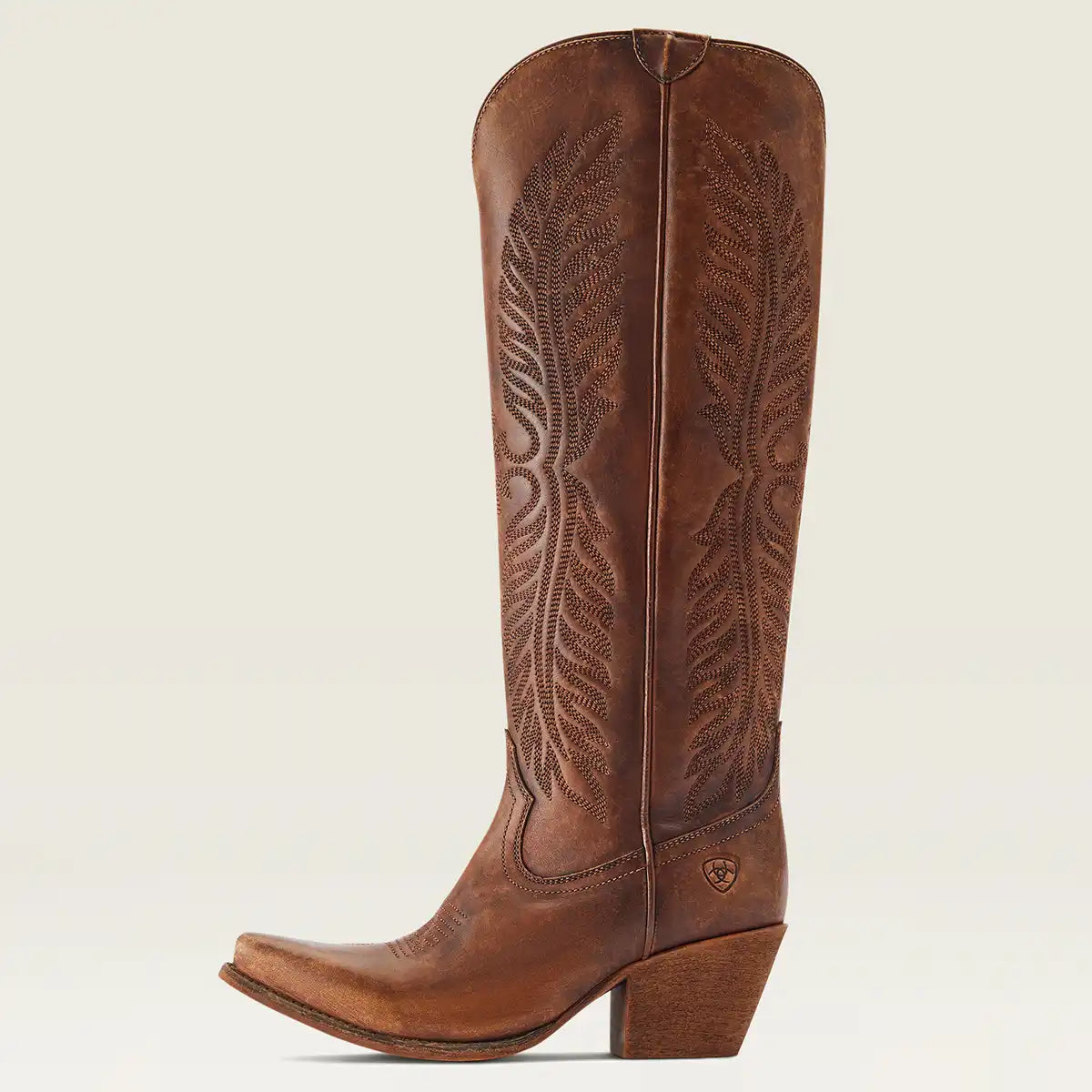 A single brown leather Ariat cowgirl boot with decorative tooling on the shaft, shown in profile against a light beige background.