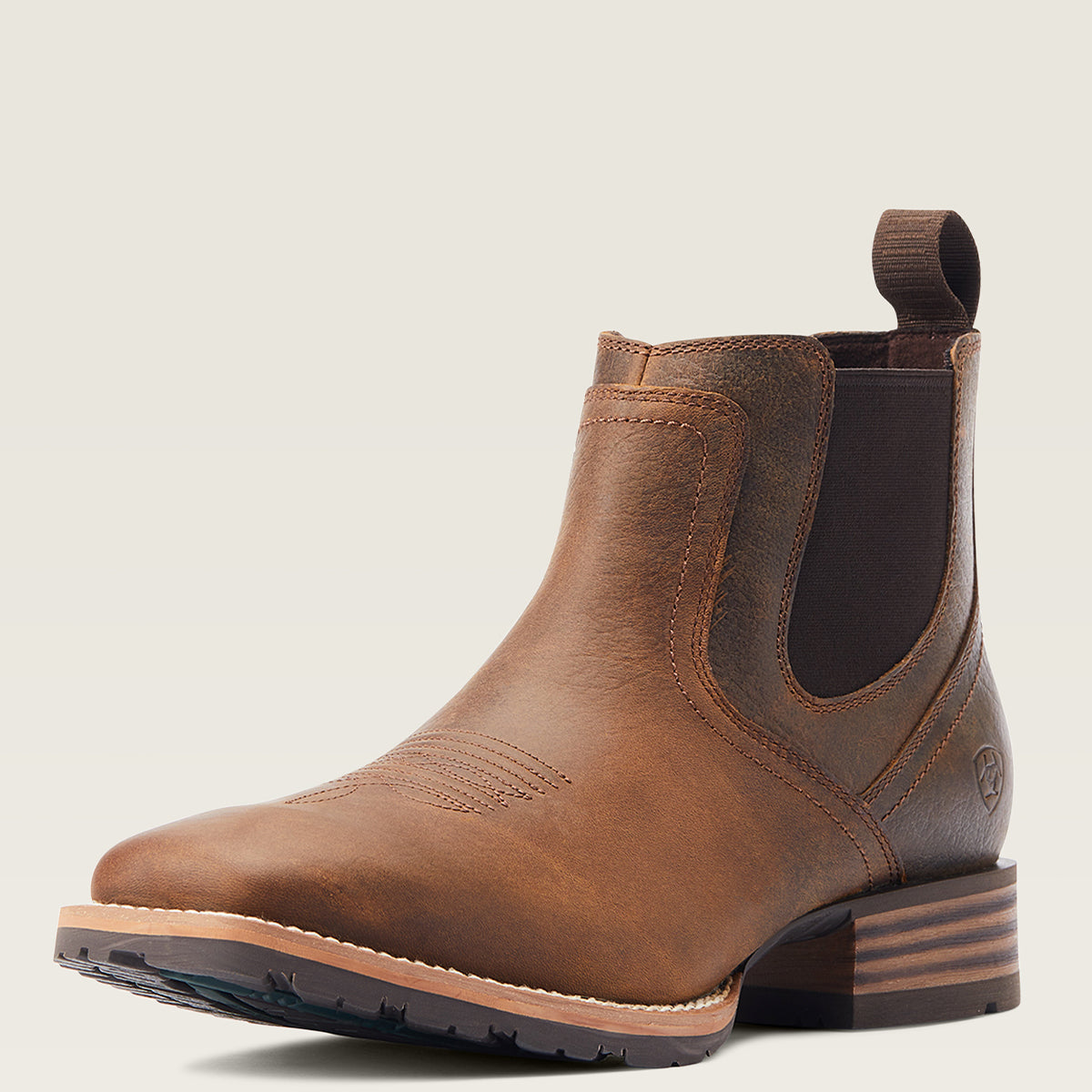 Ariat men's brown leather ankle square toe boot with elastic side panels and a pull tab, shown from a three-quarters angle on a light beige background.