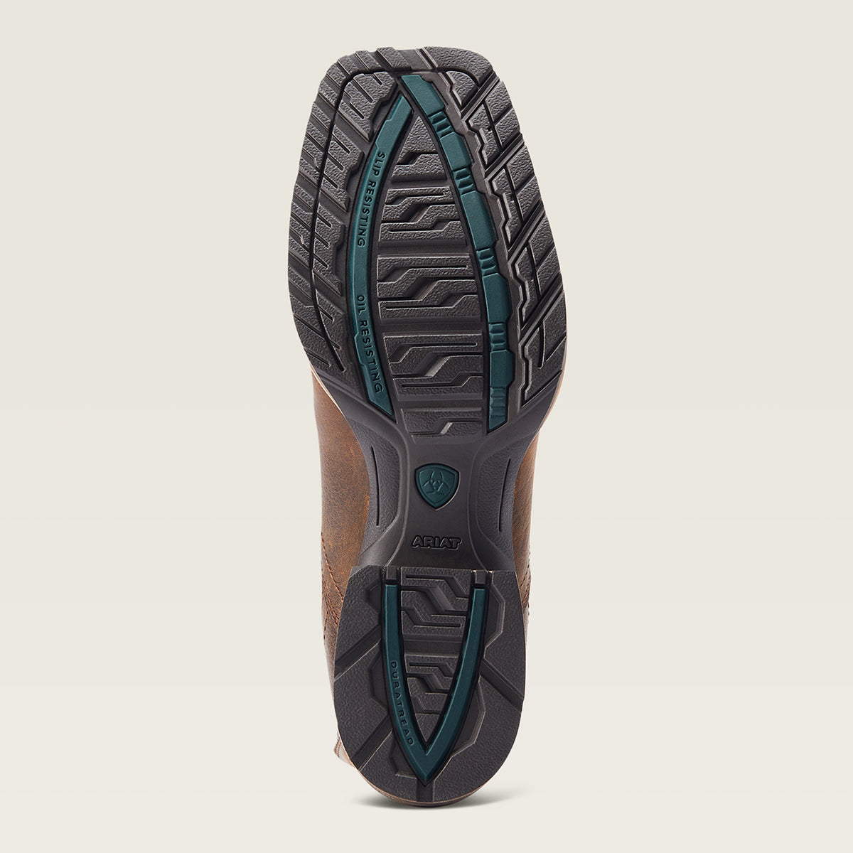A close-up of the Ariat outsole of a brown leather boot, showing a dark gray tread pattern with teal-green accents and the Ariat logo.