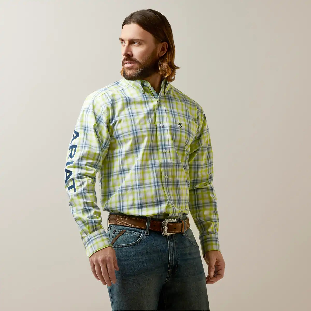 Man wearing a green plaid Ariat shirt with text on sleeves against a plain background.