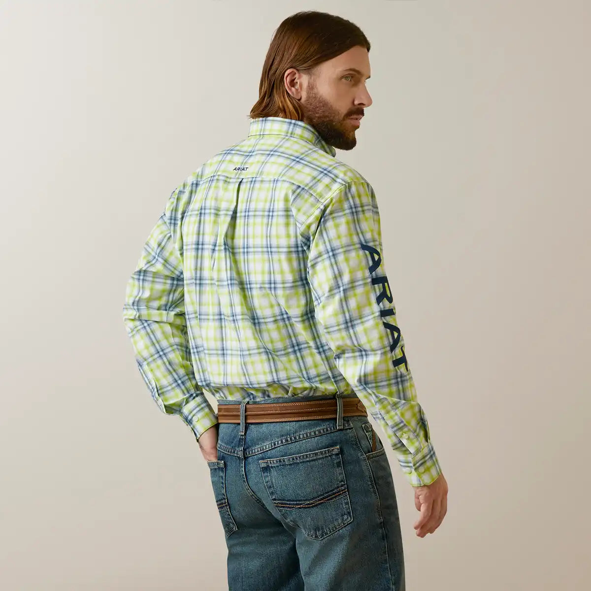 Man wearing a green plaid shirt with Ariat branding on a beige background.