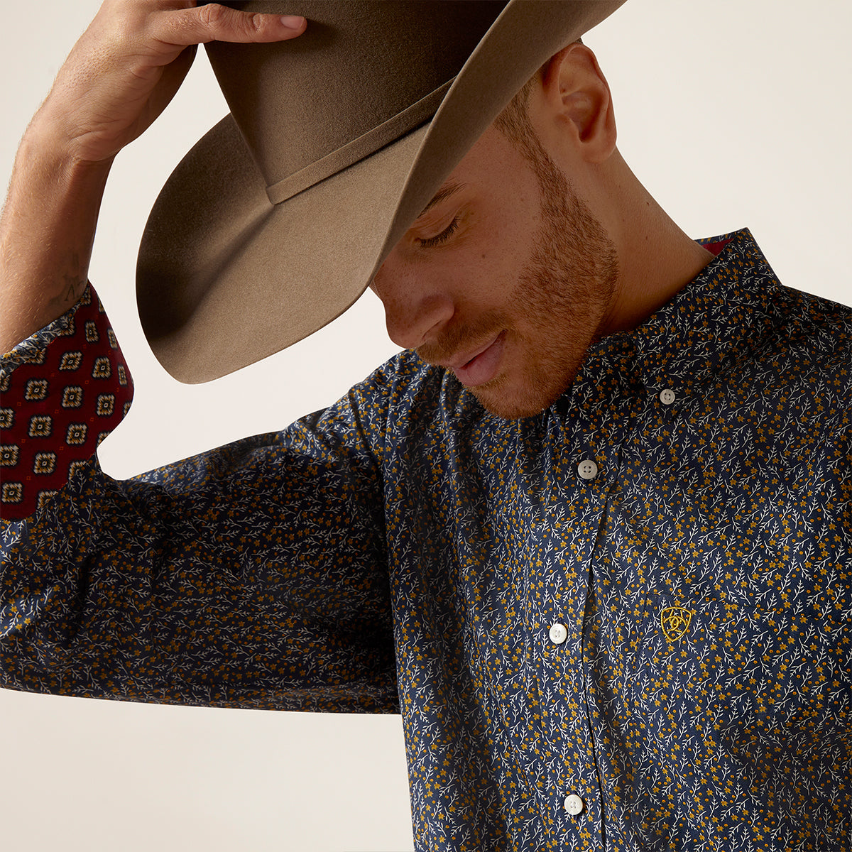 Close-up view of a man wearing the Ariat Men's Wrinkle Free Kolson Deep Pacific floral shirt with turned-up red geometric contrast cuffs.