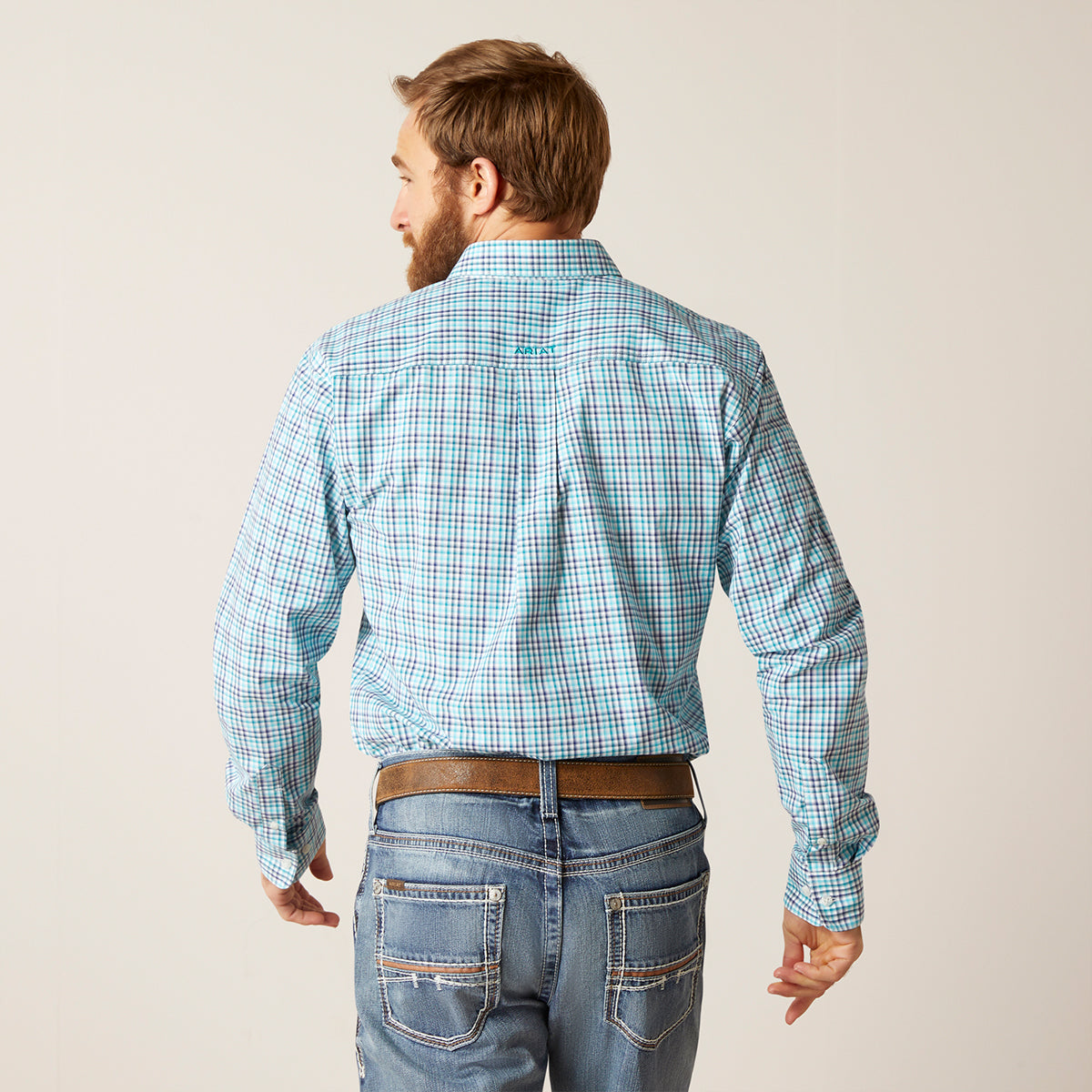 Man wearing a blue plaid shirt and jeans on a plain background.