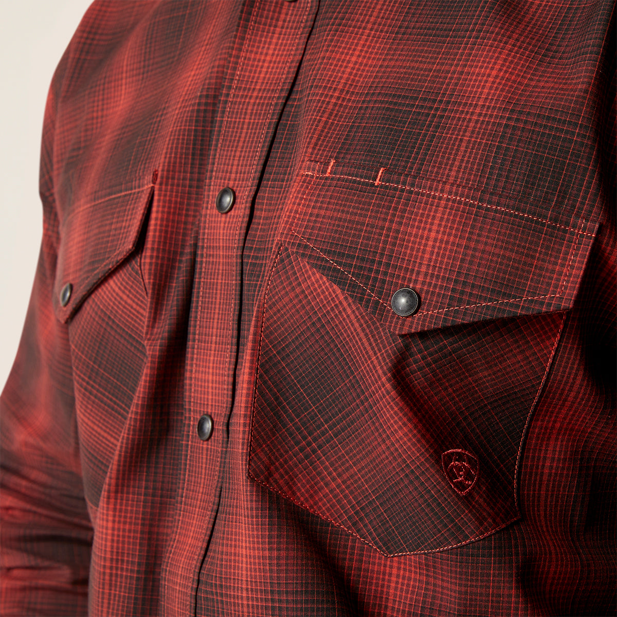 Close-up of a red and black plaid western-style button-up shirt with chest pockets and dark snap buttons.