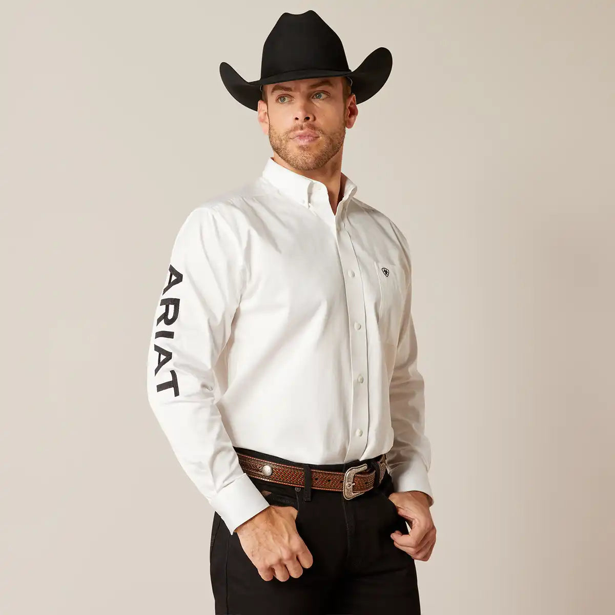Man wearing a white Ariat shirt and black cowboy hat against a plain background.