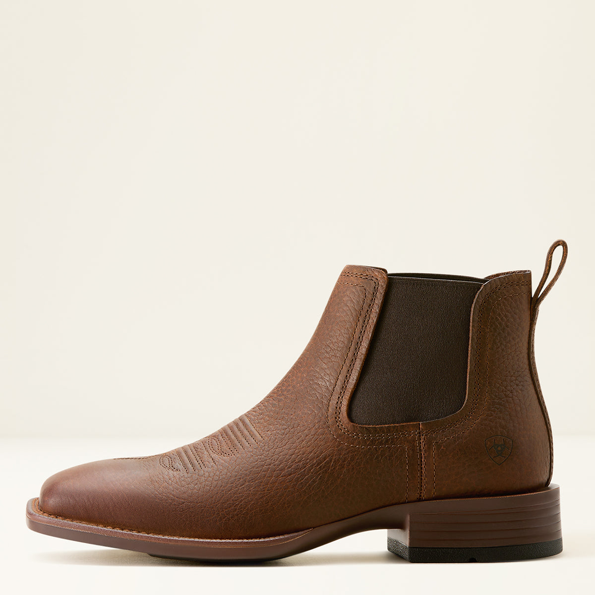 Ariat men's brown leather Chelsea ankle square toe boot with a pebbled texture, elastic side panels, and a low block heel, shown in profile against a light cream background.