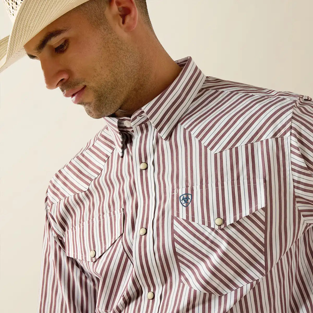 Man wearing a red and white striped shirt with a logo on a beige background.