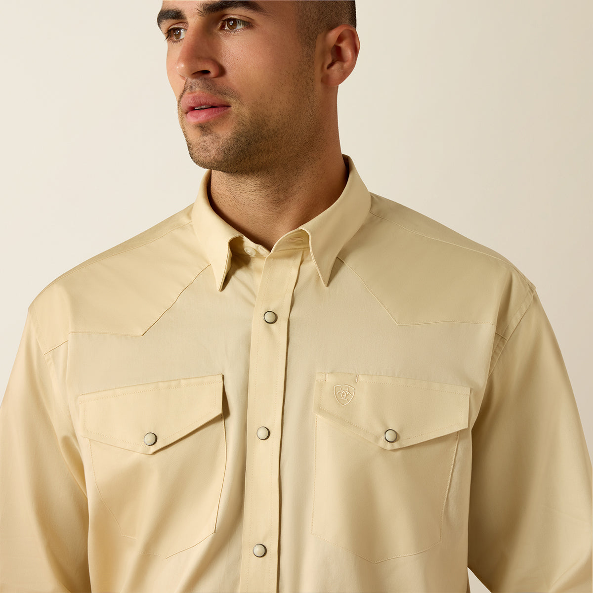 Close-up view of a man wearing the Ariat Men's Creme Brulee light tan long sleeve Western snap shirt with snap flap pockets.