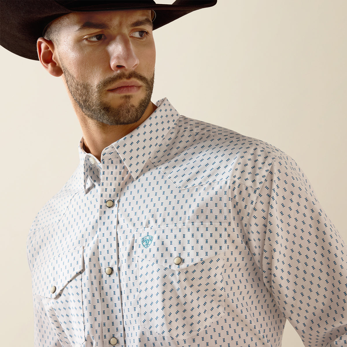 Man wearing a patterned shirt and cowboy hat against a beige background.