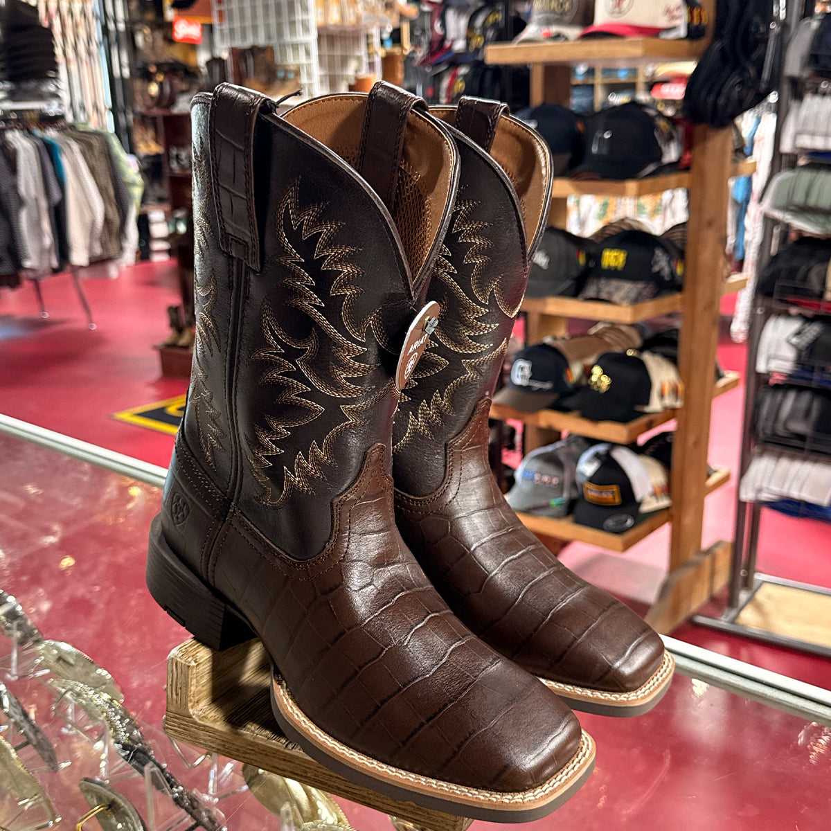 Pair of Ariat brown croc print western boots on a display stand in a western store with hats in the background.