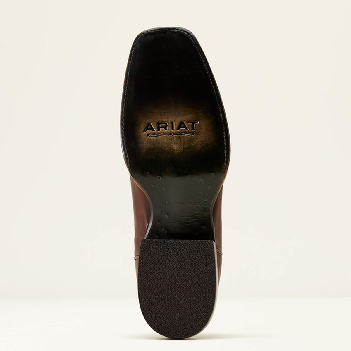 Close-up of a boot sole with 'Ariat' branding on a beige background.