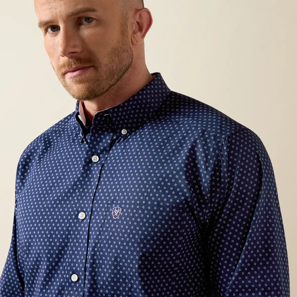 Close-up upper torso view of the Ariat navy geo print shirt highlighting the button-down collar and chest pocket with light pink logo embroidery.