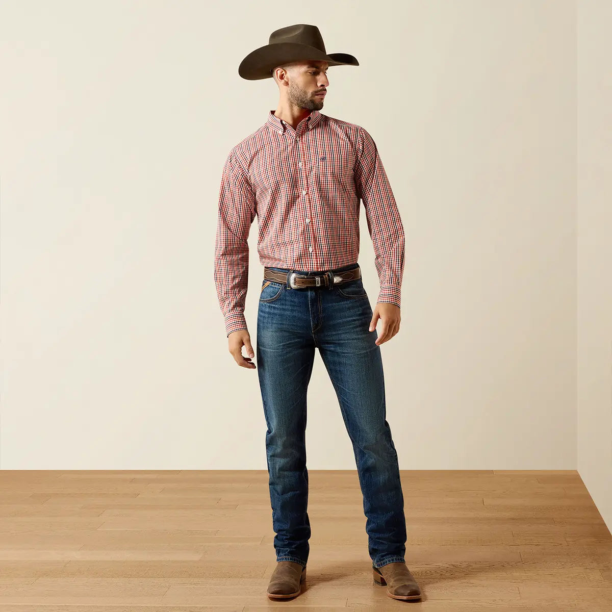 Full-body studio lifestyle view of the male model wearing the Ariat Ketchup small check shirt tucked into dark wash jeans with a Western belt and boots.