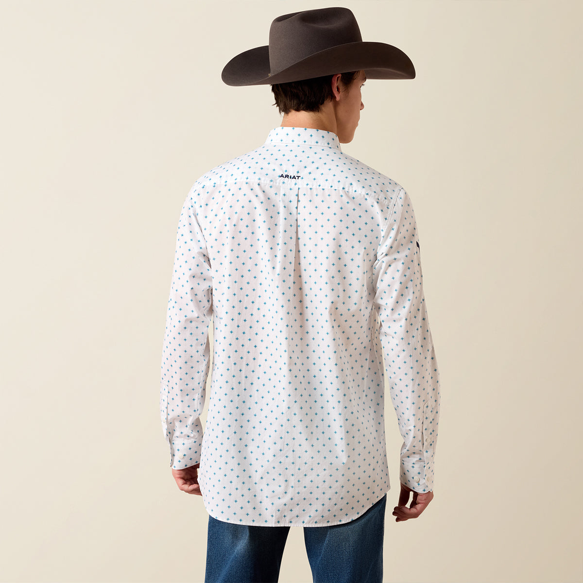 Back view of a man wearing the Ariat Men's Team Emory white printed long sleeve fitted shirt with cowboy hat and jeans.