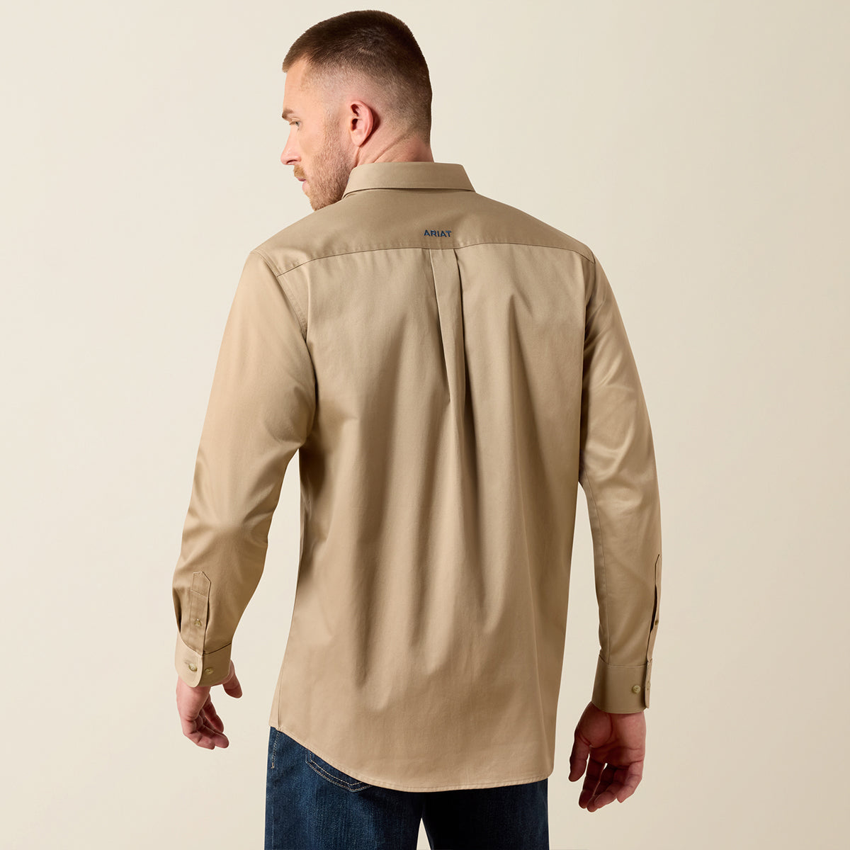 A man wearing a tan long-sleeve button-down shirt, shown from the back, paired with blue jeans against a plain beige background.