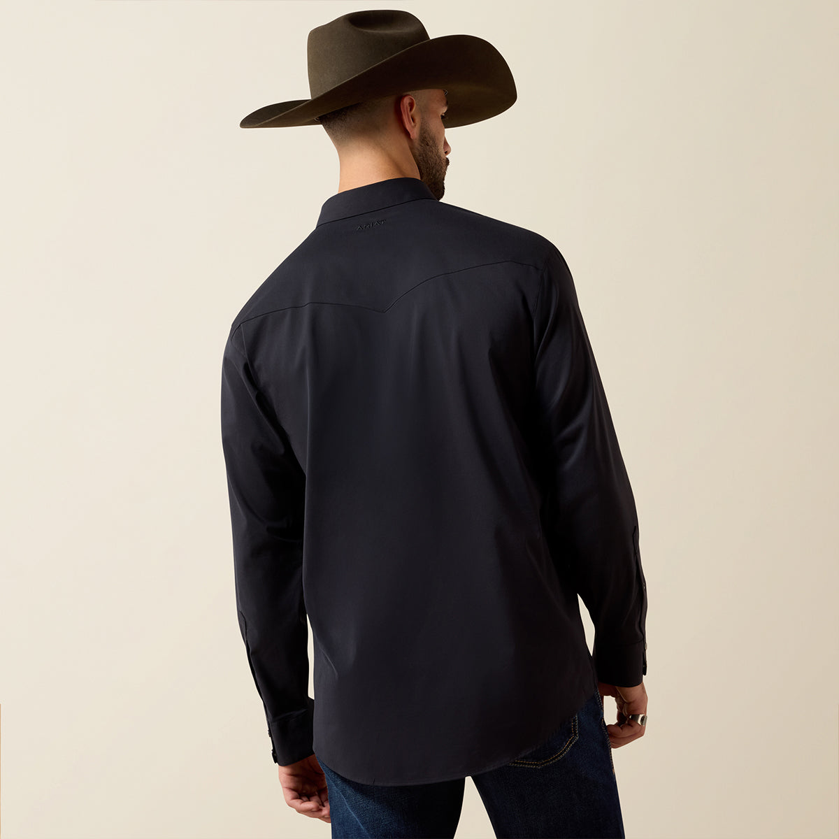 A man wearing a black long-sleeve western shirt and a brown cowboy hat, shown from the back against a plain beige background.