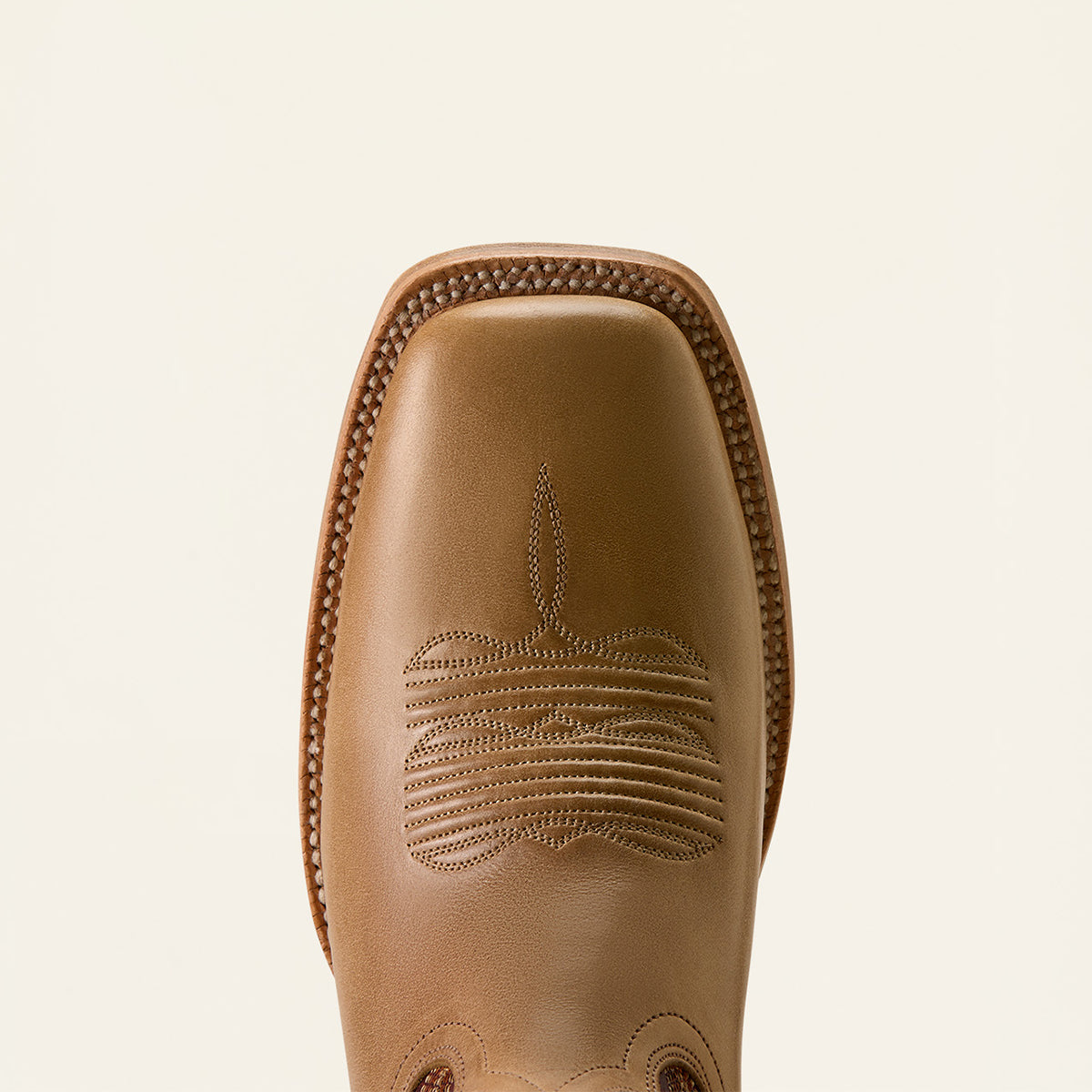 A close-up top-down view of a tan leather boot square toe with decorative stitching and a square vamp, shown against a light cream background.