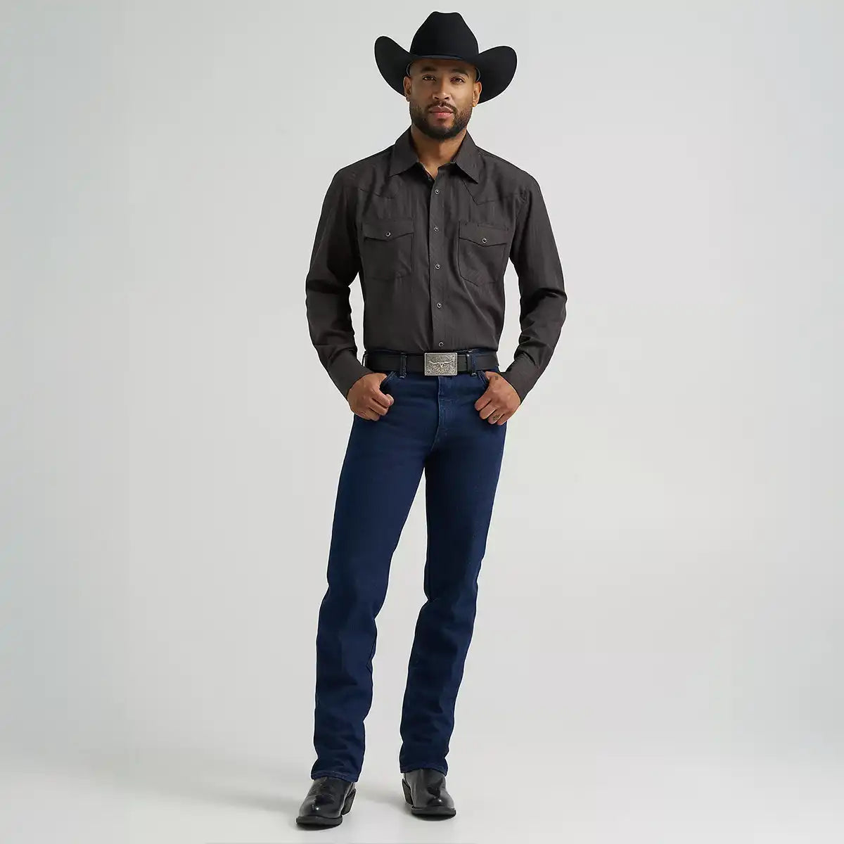 Full length view of a man wearing Wrangler Men's Cowboy Cut Silver Edition slim fit dark denim jeans with cowboy boots and hat.