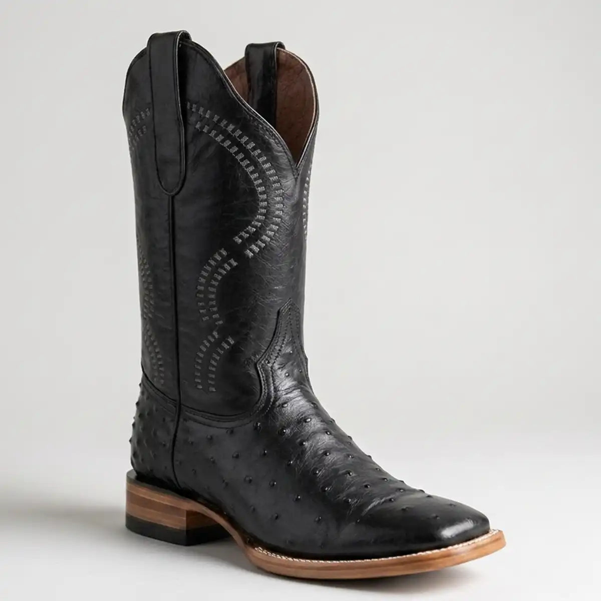 Men's black ostrich print leather square toe cowboy boot on light grey background.