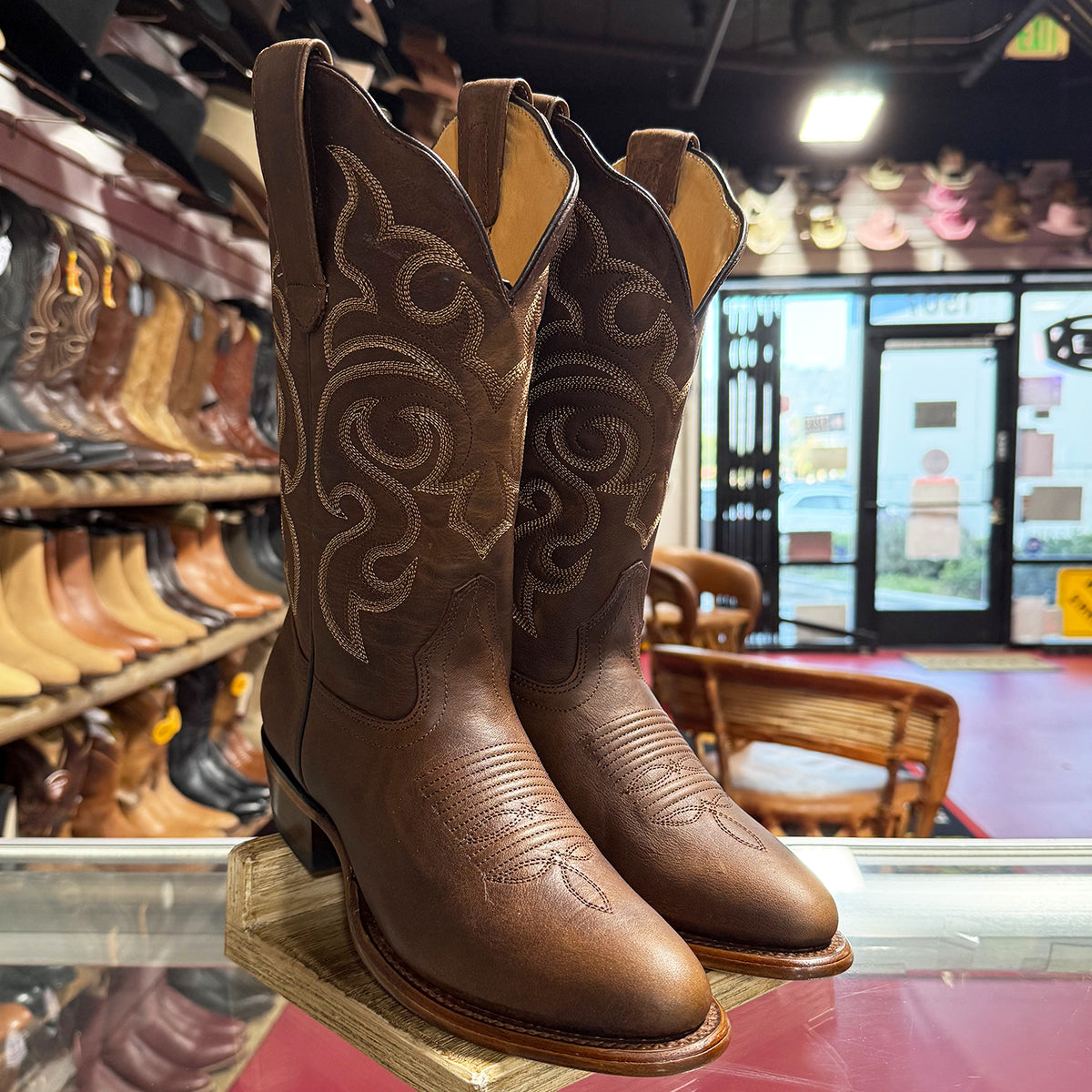 A pair of women's Los Altos brown leather cowboy boots with decorative western stitching, displayed on a wooden stand inside a western store.