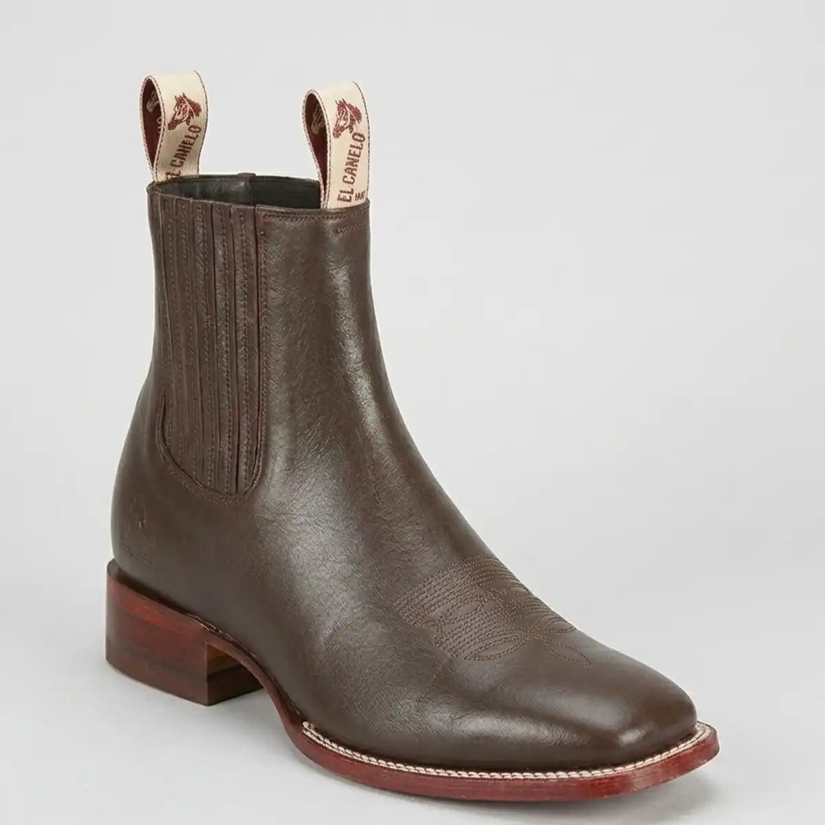 A dark brown leather Chelsea boot with a low block heel and elastic side gore, shown on a light gray background. The pull tabs are branded with 'EL CANELO'.