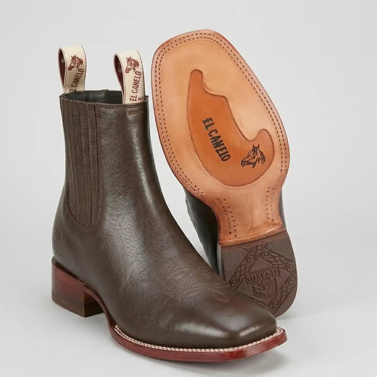 A pair of dark brown leather western boots shown on a light gray background, with one boot standing upright and the other tilted to display the tan leather sole and pull tabs.