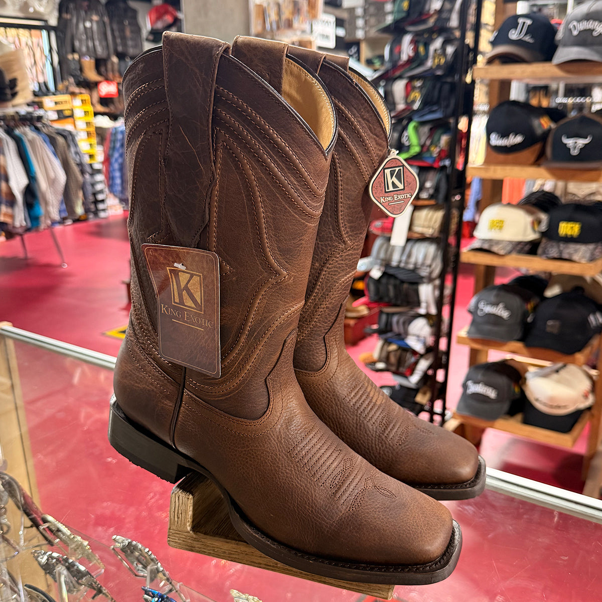 King Exotic men's brown leather western square toe boots displayed on a wooden stand inside a retail store.
