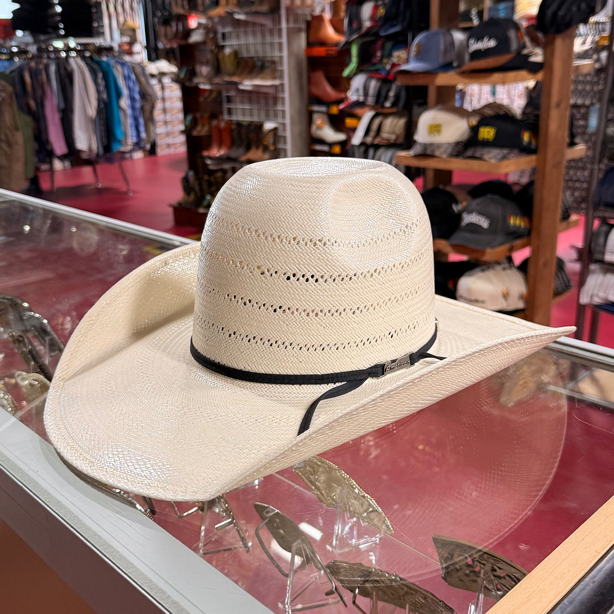 American Hat Co straw cowboy hat with a black band, displayed on a glass case inside a western store.