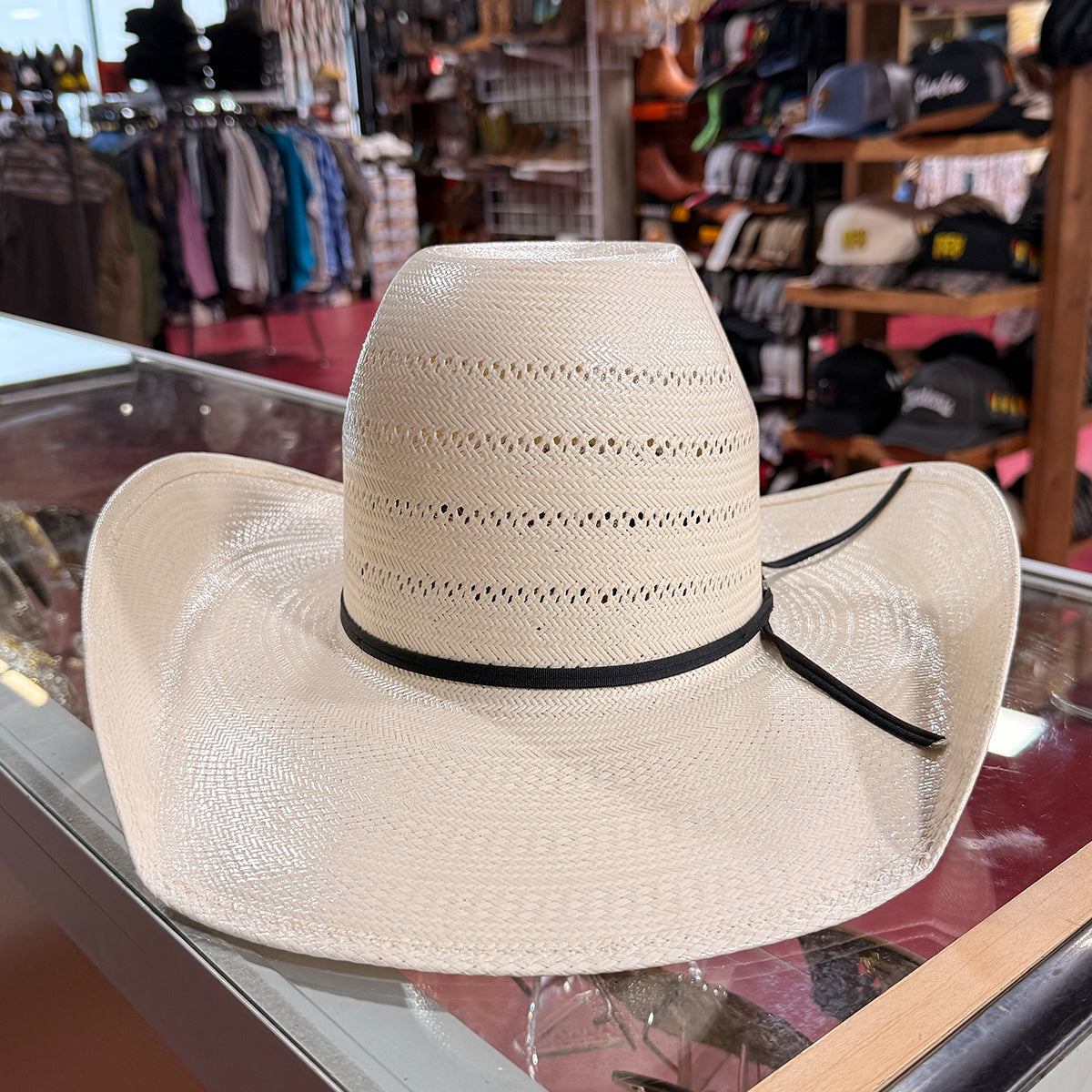 American Hat Company straw western hat with a black ribbon band, displayed on a glass countertop inside a western store.