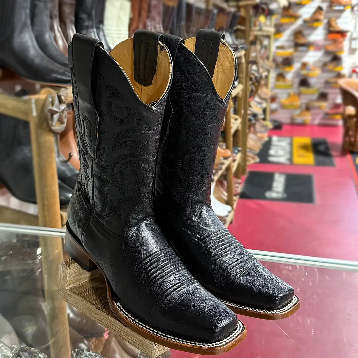 In-store display view of the pair of Los Altos men's black smooth ostrich belly square toe cowboy boots on a wooden stand.