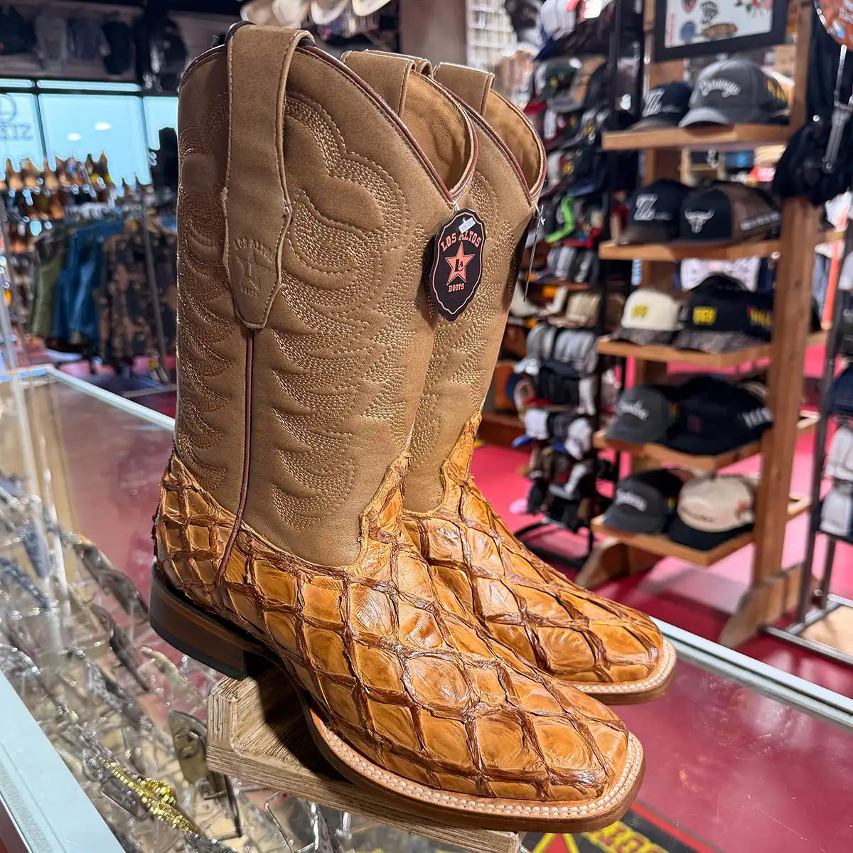 A pair of Los Altos Pirarucu tan western boots with a stitched shaft, displayed on a glass case inside a western store.