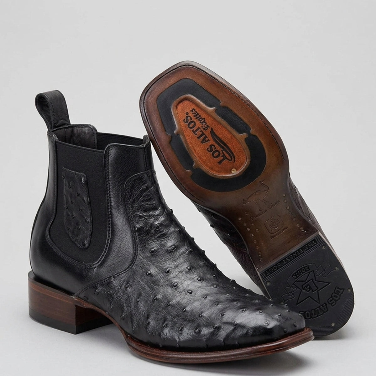 A pair of Los Altos men's black ostrich leather cowboy boots, shown on a light gray background. One boot is standing upright, displaying its black pull tab, side gusset, and stacked block heel.