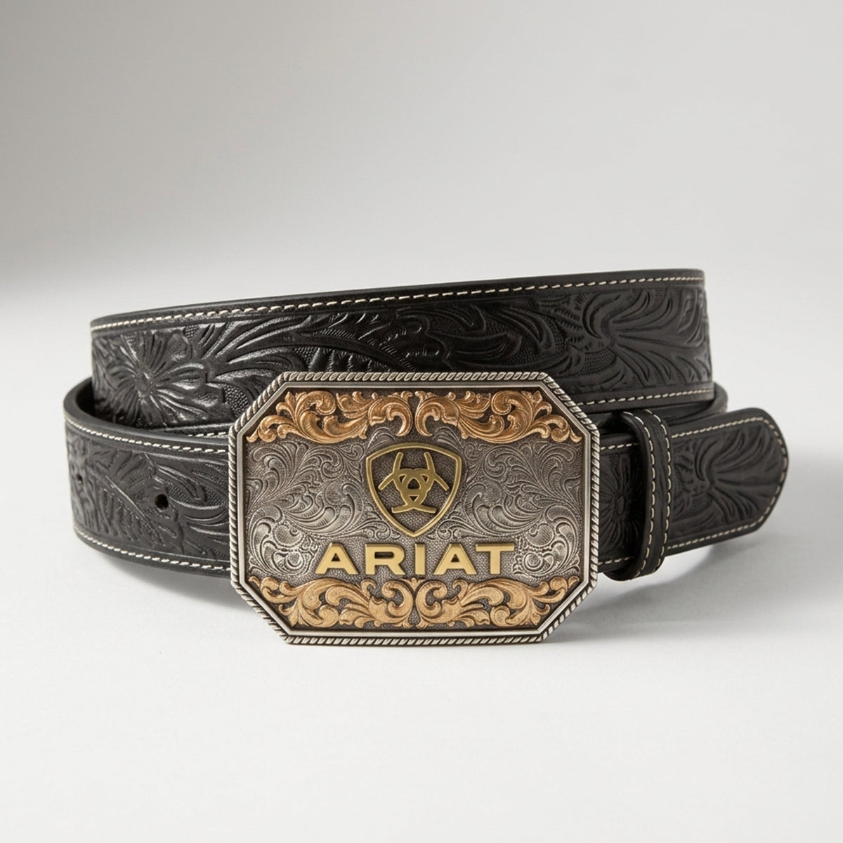 Ariat Men's black embossed floral leather belt featuring a large silver and gold two-tone Western buckle with the Ariat shield logo.