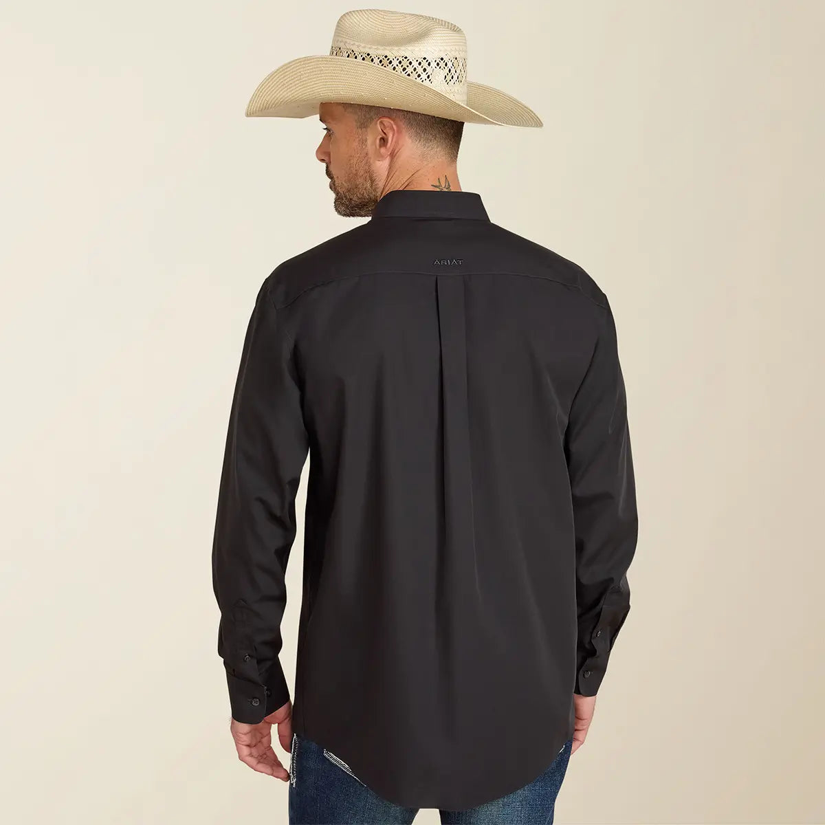Rear view of the model showing the back fit, box pleat, and tonal black Ariat logo embroidery on the back collar of the black shirt.