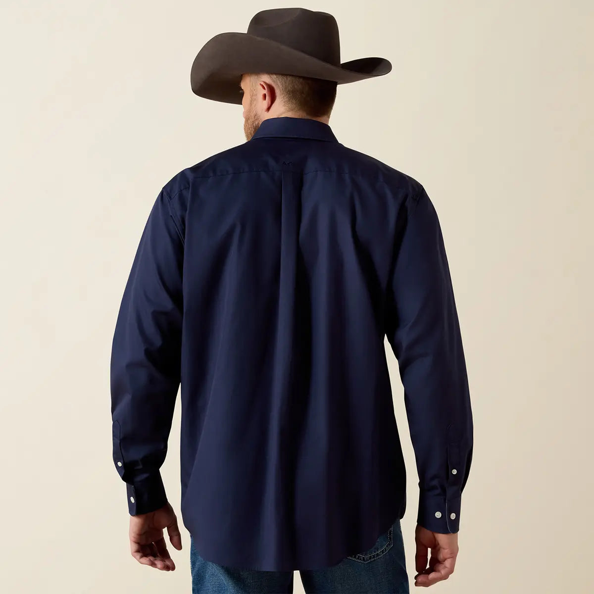 Rear view of the model showing the back fit, box pleat, and tonal Ariat logo embroidery on the back collar of the navy blue shirt.