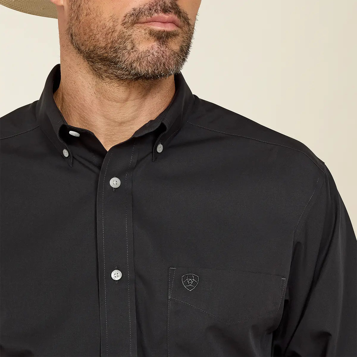 Close-up of the collar and chest pocket on the black Ariat shirt highlighting the white buttons and tonal black shield logo embroidery.