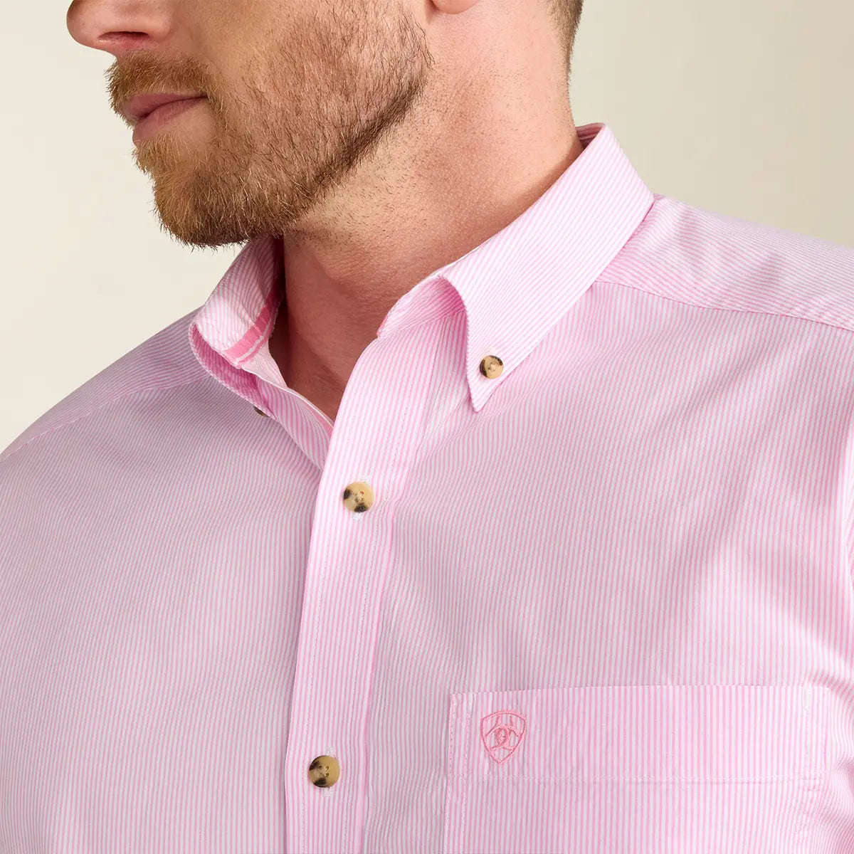 Close-up view of the collar and chest pocket on the Ariat Dayne shirt highlighting the fine Prism Pink yarn-dye stripes, tortoiseshell buttons, and tonal pink shield logo.