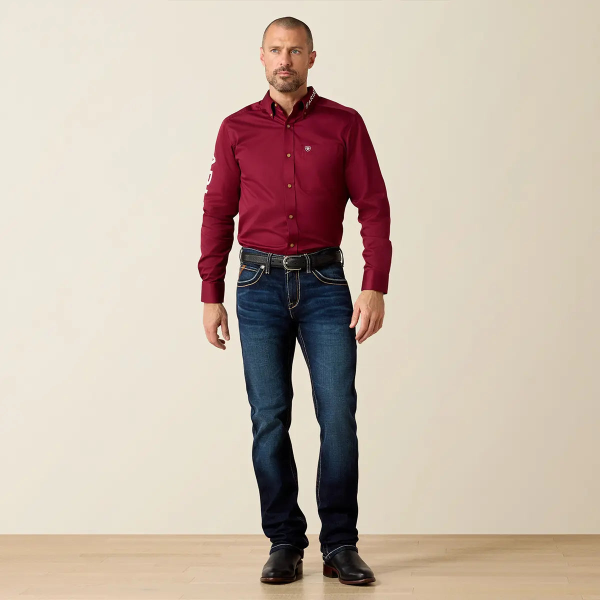 Full-length lifestyle shot of a model standing in Ariat Men's M7 Rocker Concord Doge Blue jeans paired with black leather boots.