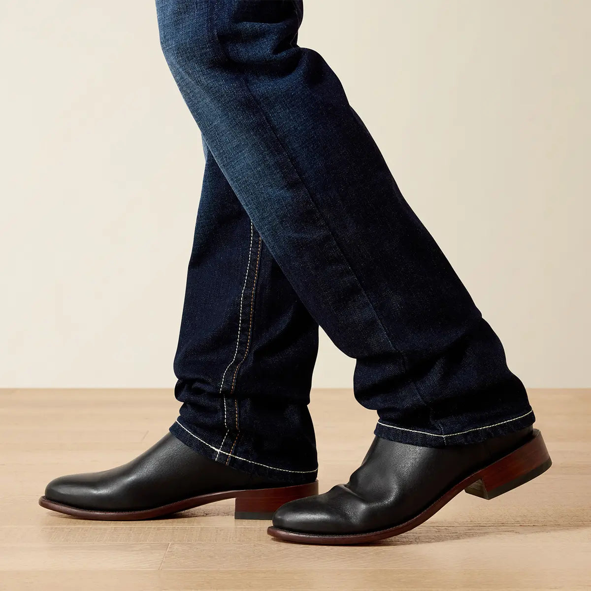 Close-up shot of the lower leg on the Ariat M7 Rocker Concord jeans showing how the 17.75" leg opening stacks over black leather cowboy boots.