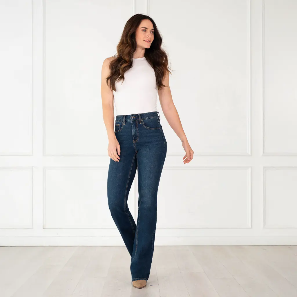 Full-length front view of a model wearing Rock & Roll Denim Women's Sculpted dark high rise bootcut jeans with a white tank top.