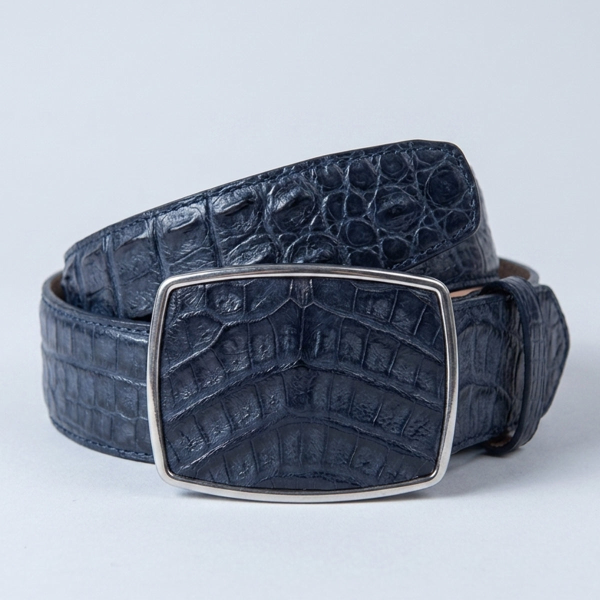 A Los Altos men's blue caiman hornback leather belt with a silver-toned rectangular buckle, coiled on a light gray background.