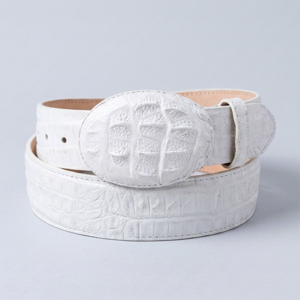 Los Altos white crocodile hornback leather belt with a large oval buckle, coiled on a light gray background.